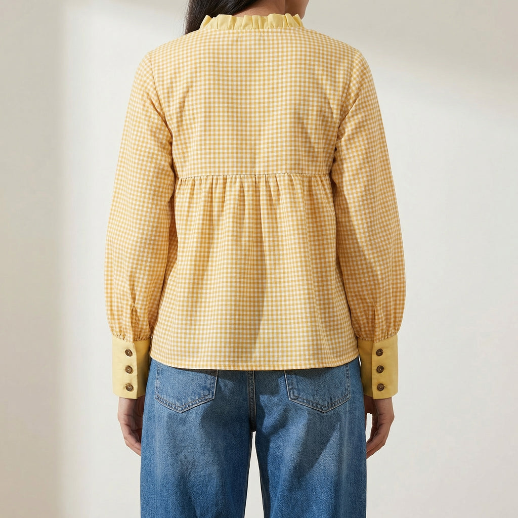  wearing a yellow checkered blouse and blue jeans against a plain background