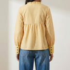  wearing a yellow checkered blouse and blue jeans against a plain background