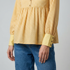 Person wearing a yellow checkered blouse and blue jeans on a gray background