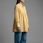 Woman wearing a yellow checkered dress with blue jeans on a gray background